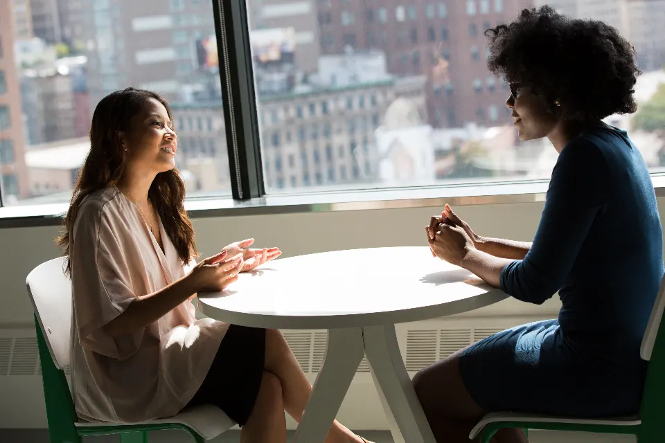 Two professionals in conversation at a table by a window overlooking city buildings