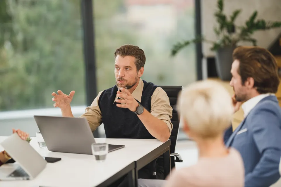 A professional team in discussion around a meeting table with laptops